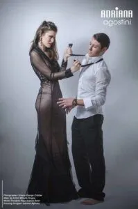 Black-and-white campaign portrait of a woman in a sheer couture dress being fitted by a tailor